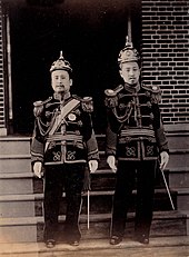 Photographie de deux hommes debout faisant face au photographe. Ils portent des uniformes militaires de cérémonie.