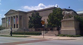 Photo of a large building with Grecian-style pillars, trees, and a lion statue nearby