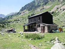 Maison à étage, rez-de-chaussée en pierres, étage en bois dans un paysage verdoyant de montagne.