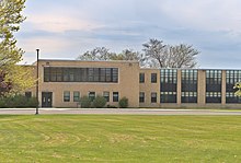 A sandstone colored, modernist brick school building with tall black windows