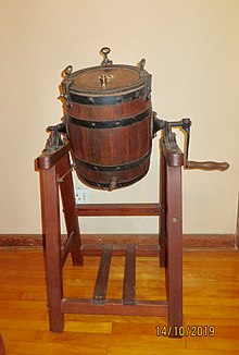 Barrel-shaped oak container, rotating on pine framework or stand. Used in a farm environment to manually agitate cream to produce butter and buttermilk, the byproduct of butter production.