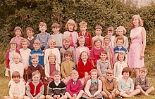 Group of seated children next to a standing woman