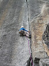 Kletterer in steiler Wand, der sich an einem Riss hält und mit den Füssen dagegen stemmt