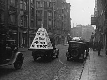 Photographie en noir et blanc de trois automobiles, dont l'une porte un cône de grande taille indiquant « victime de l'impôt ».