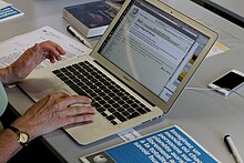 Photo d'un ordinateur avec un brouillon de trois lignes d'Alice Recoque sur Wikipédia. Aux alentours, des livres, des feuillets de publications, un code wifi et un livret pour guider dans la rédaction.