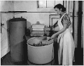 Woman turning the nozzle on hose to washing machine with wringer (Rural Electrification Administration)