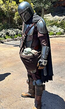 Comédien portant un costume de Din Djarin accompagné de Grogu à Star Wars: Galaxy's Edge à Disneyland.