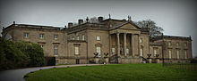 A mansion with two adjacent wings, with a gravel drive and lawn in front