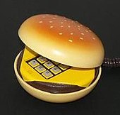 Photographie d'une forme de hamburger entrouvert laissant apparaître le clavier d'un téléphone jaune.