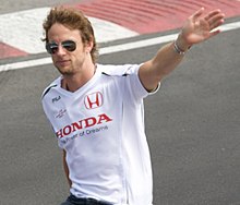 Photo de Jenson Button, en t-shirt Honda et lunettes de soleil, levant la main gauche