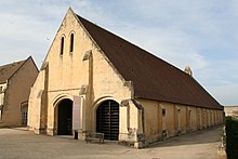 Photographie en couleurs d'une large grange en calcaire avec un toit à deux pans, et deux portes voûtées.