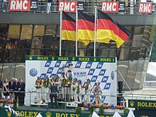 A group of drivers on a podium with three German flags raised above them