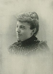 B&W portrait photo of a woman with hair in an up-do, wearing a dark blouse.