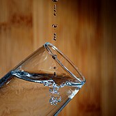 Agua goteando en un vaso, mostrando gotas y burbujas