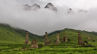 À flanc de montagne des tiges de pierres se dressent devant de hauts nuages.