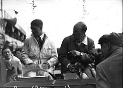 Photo de deux hommes assis sur la carrosserie de leur voiture.