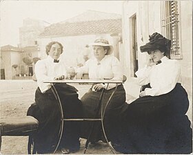 Photo of three women dressed in Victorian skirts and blouses, seated together around a small table outdoors