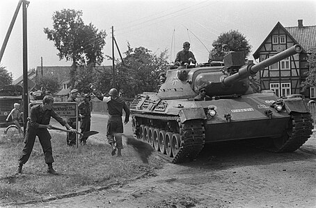 Dutch soldiers repairing the damage from armoured vehicles as a West German Leopard 1 pass during the "King's Gambit" exercise in Germany, 1968.