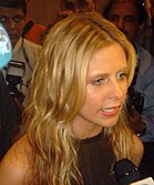 Sarah Michelle Gellar speaking into a microphone in a dark sleeveless top