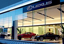 Showroom ô tô với một chiếc coupe cùng hai chiếc sedan nằm phía sau tấm kính, bên trên là dòng chữ "Lexus".