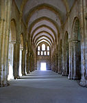 A corridor enclosed by large pillars, which ends with a small doorway.