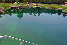 A pond with bluish-green water, several buoys and recreational facilities around it, seen on a cloudy day