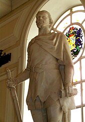 Kip moža v tuniki in kratkem ogrinjalu, prekrižanem na desni rami, iz belega kamna. Kip stoji v zaprtem prostoru s hrbtom ob obokanem oknu, ima navzdol obrnjen meč v desni roki in zvitek v levici.