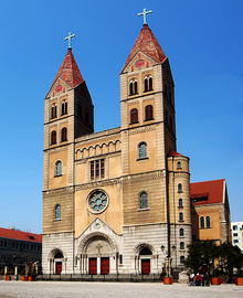 A cathedral in neo-Romanesque style, with twin spires topped with crosses, stands against the blue sky.