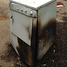 Una secadora de ropa blanca con los lados carbonizados sentada al aire libre en el pavimento.