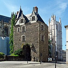 Grande bâtisse en pierre surmontant un porche ; au second plan, la cathédrale.