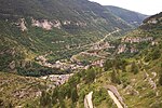 A small village lies almost hidden by trees in a narrow valley between steep sided mountains.