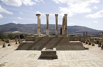 View of the dais of a temple, with an altar standing on a square below and a series of reconstructed columns standing at the head of a set of steps leading up to the top of the dais