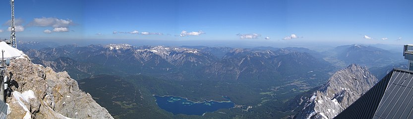 Panorama toward Germany - mountains of Ammergauer Alpen (Prealps) in the North of Zugspitze. And in the right: Mountain range Estergebirge with summit Wank behind the rocky peak, the valley of river Loisach and town Garmisch-Partenkirchen