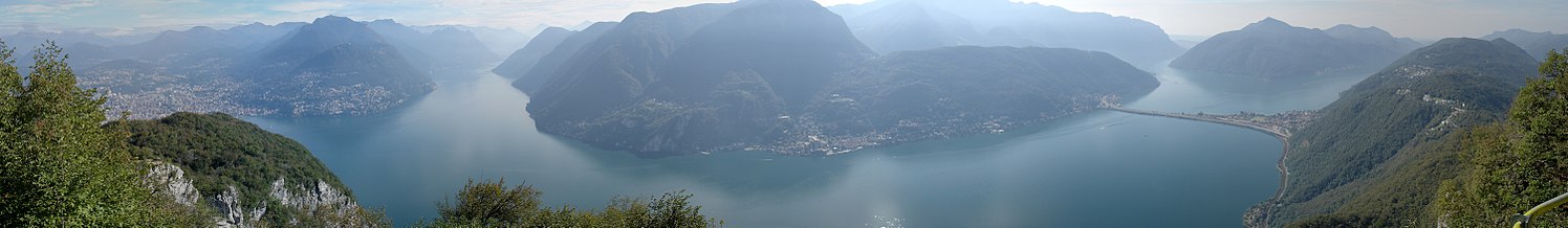 Vido de lago Lugano de monto San Salvatore, kun Lugano maldekstre kaj la akvobaraĵo de Melide dekstre