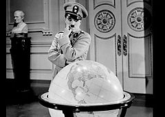 Photographie en noir et blanc d'un homme légèrement petit à la moustache carrée et aux gros sourcils portant un uniforme militaire à l'insigne XX. Il regarde avec envie une mappemonde d'environ 60 cm de diamètre.