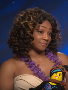 A Black woman in a blue dress in front of dark blue curtains