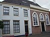 Pand met gepleisterde gevel met rechte kroonlijst, een geheel met kerkgebouw vormend