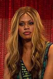 Photographie de Laverne Cox sur fond rouge. Elle porte du maquillage rafiné et un débardeur.