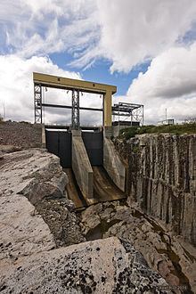 Image d'un ouvrage en béton avec des vannes et dont la partie la plus basse ressemble à un saut à ski qui mène à un corridor en roc.