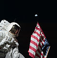 Harrison Schmitt posa con la bandera estadounidense y la Tierra en segundo plano durante el primer EVA del Apolo 17. Eugene Cernan se ve reflejado en la visera del casco de Schmitt.