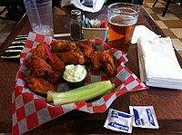 Buffalo wings con acompañamiento de queso azul, servidas con una cerveza rubia.