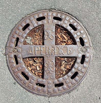 Manhole cover with the inscription ДРЕНАЖЪ (DRAINAGE), made in Russian pre-revolutionary spelling, on the territory of the Peter the Great Hospital in St. Petersburg