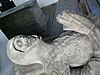 Stone effigy of a knight in armour, chest up, face damaged, hands clasped in prayer.