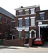 A brick building in three storeys and three bays, with a doorway surrounds by pilasters and a pediment