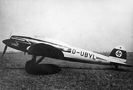 Photographie en noir et blanc d'un avion à hélice vu de côté, posé sur l'herbe, portant une croix gammée sur la queue.
