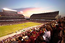 a crowd of people watch a football game at a three-tiered stadium