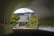 Bâtiment de forme traditionnelle des maisons japonaises dans un lieu de verdure mais avec verre et structure en métal.