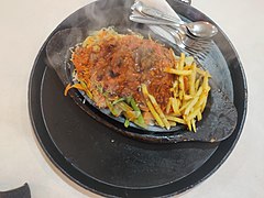 Chicken sizzler disajikan dengan suhu tinggi di dalam peralatan kayu yang berat.