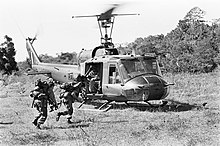 Black and white photograph of soldiers running towards a helicopter