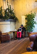 Homme lisant un journal dans un bar de la place Pigalle (31027293286).jpg